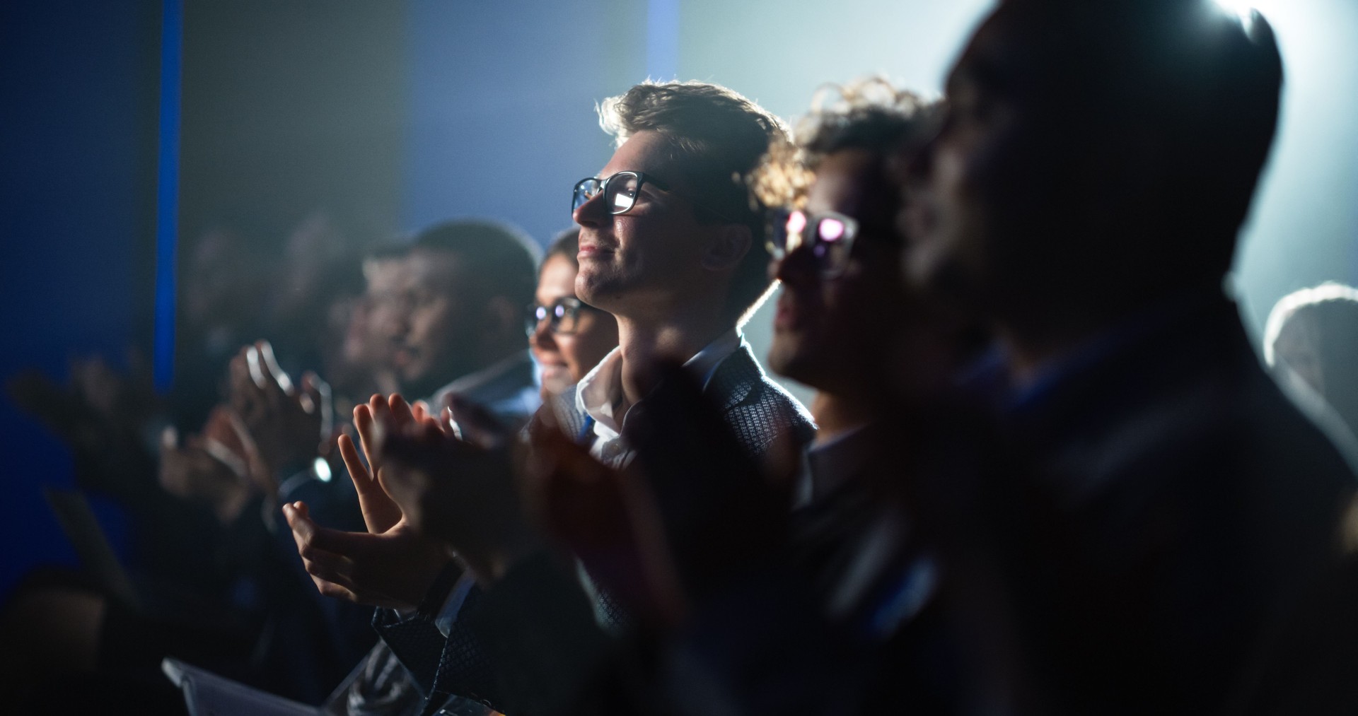 Young Man Sitting in a Crowded Audience at a Business Conference. Male Attendee Cheering and Clapping After a Motivational Keynote Speech. Auditorium with Young Successful Businesspeople.
